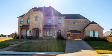 Large two-story brick house with a driveway and garage under bright sunlight.