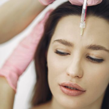 Women looking down while a syringe is hold close to her forehead 