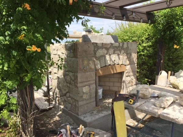 Stone outdoor fireplace under construction in a garden setting.