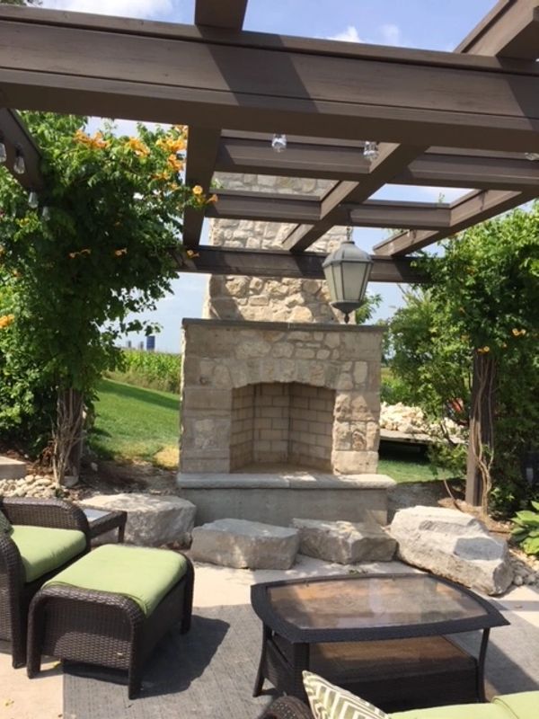 Cozy outdoor seating area with stone fireplace and greenery under a pergola.