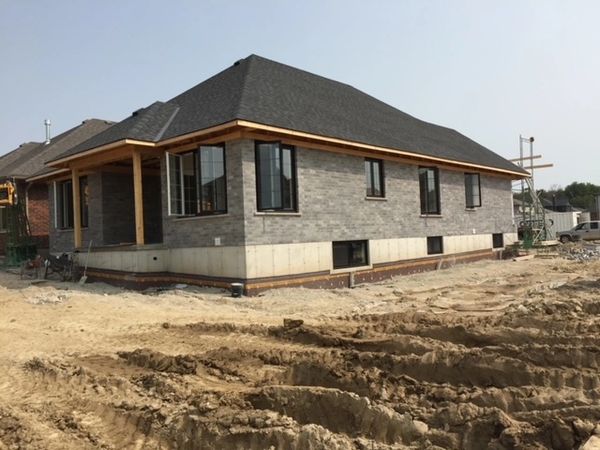 Newly constructed single-story house with gray brick exterior and black roof.