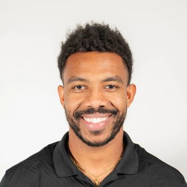Smiling man with a beard and curly hair in a black polo shirt.