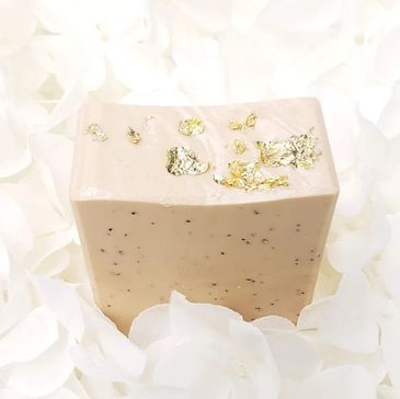 Luxurious handmade soap with gold leaf and ground apricot seeds on top of a white flower bed.