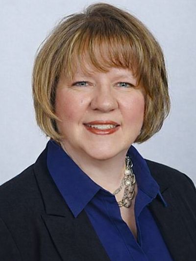 Professional woman with short hair wearing a blue shirt and black blazer.