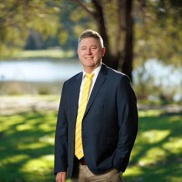 Man in a suit with a yellow tie smiling outdoors.