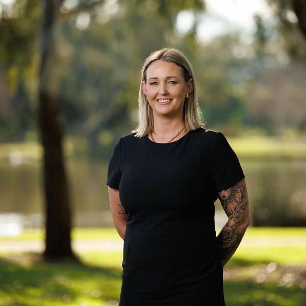 Smiling woman with tattoos in black dress outdoors.