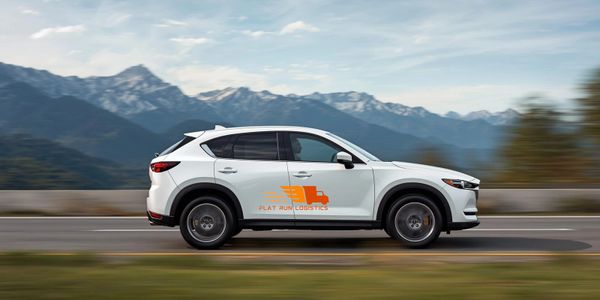 White SUV with orange logistics logo driving on a mountain road.