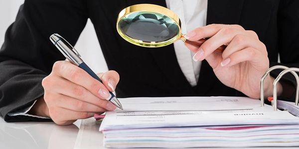Person inspecting documents with a magnifying glass and pen.