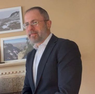 Man in suit standing indoors near framed pictures.