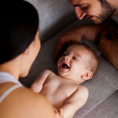 Happy baby smiling with parents on a couch.