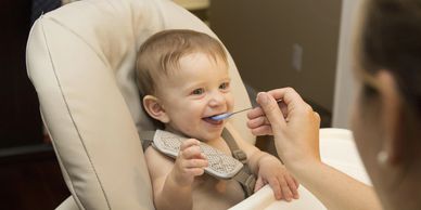 A baby happily being fed with a spoon while sitting in a high chair.