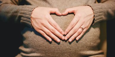 Pregnant woman making a heart shape with her hands over her belly.