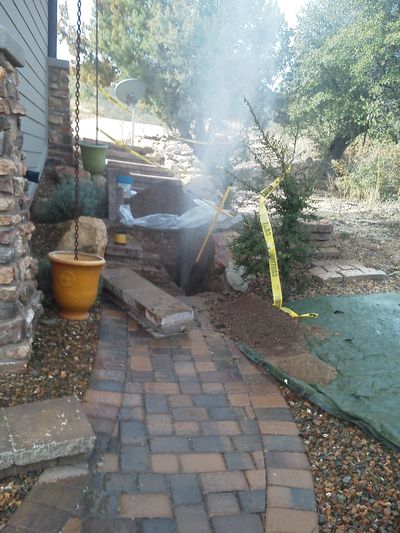 Smoke rises from a covered pit in a backyard garden area.