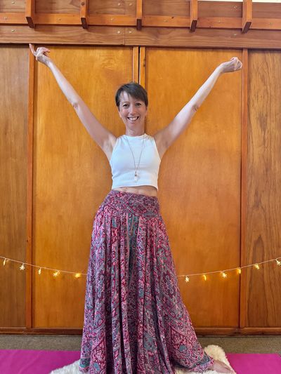 Woman smiling with raised arms in a colorful skirt and white top.