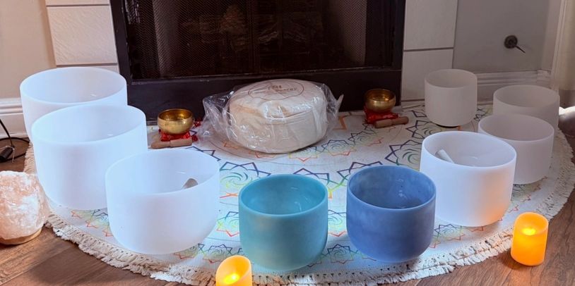 A circle of colorful singing bowls and candles arranged on a patterned mat.