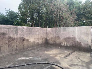 Empty concrete corner with damp stains and surrounding trees.