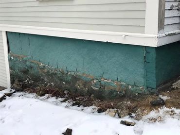 Cracked and weathered foundation wall with snow at the base of a house.