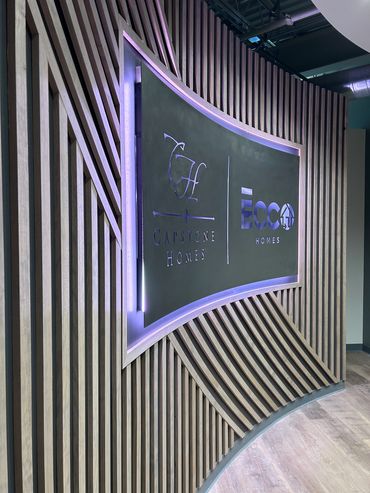 Modern curved wooden wall with illuminated Capstone Homes and ECC Homes logos.