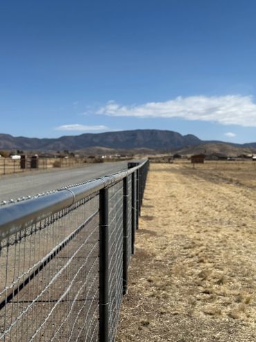 Long metal fence along a rural dirt road with mountains in the distance.