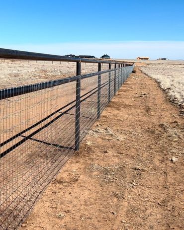 Long metal fence stretches across a dry, open landscape under a clear blue sky.