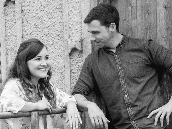 A smiling woman and a man share a moment by a rustic fence.