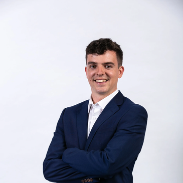 Young man in a navy blue suit smiling confidently with arms crossed.