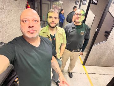 Three men posing in an indoor shooting range.