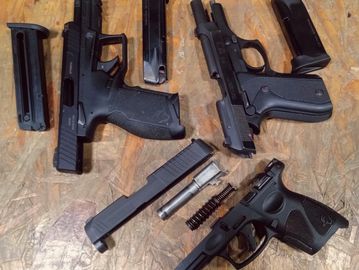 Three disassembled handguns with magazines on a wooden surface.