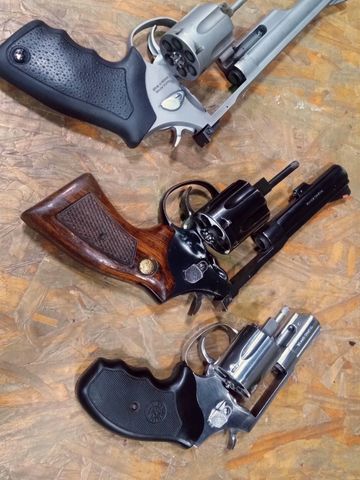 Three revolvers with different grips and finishes displayed on a wooden surface.