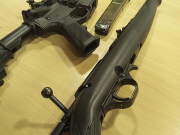 Two rifles placed on a wooden surface, one with a bolt action and the other with a magazine.