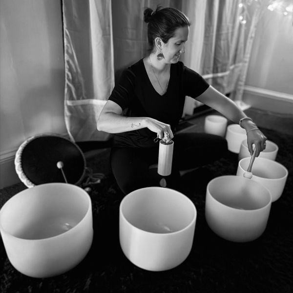 Woman playing crystal singing bowls in a serene room.