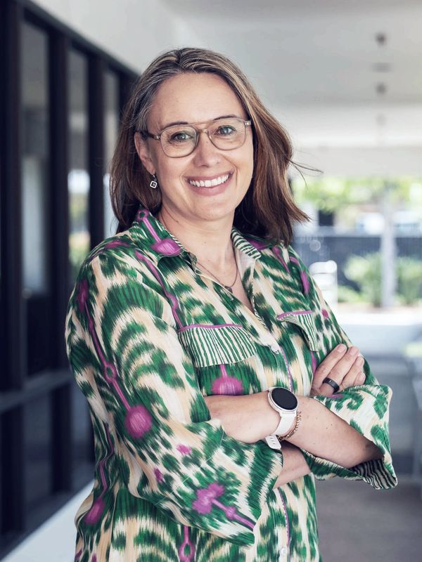 Smiling woman in glasses with patterned shirt and smartwatch, standing confidently indoors.