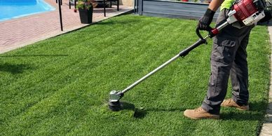 Person trimming grass near pool using a string trimmer.