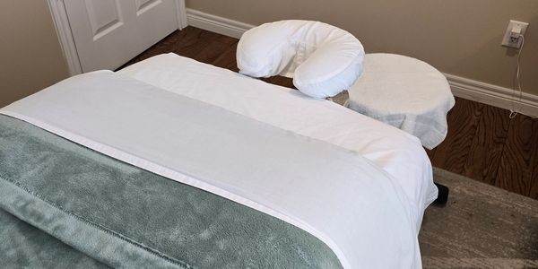 A neatly prepared massage table with soft blankets and face cradle in a calm room.