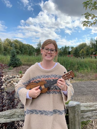 MAriah is standing outside holding a ukulele 