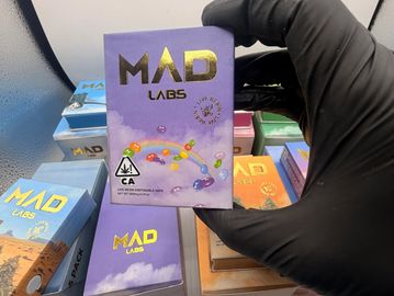 A gloved hand holds a MAD Labs product box with colorful beads on it.
