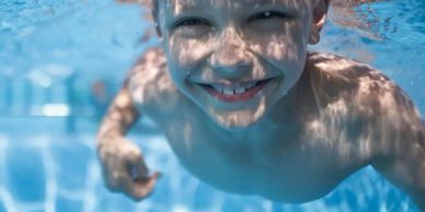 Smiling child swimming underwater in a pool.