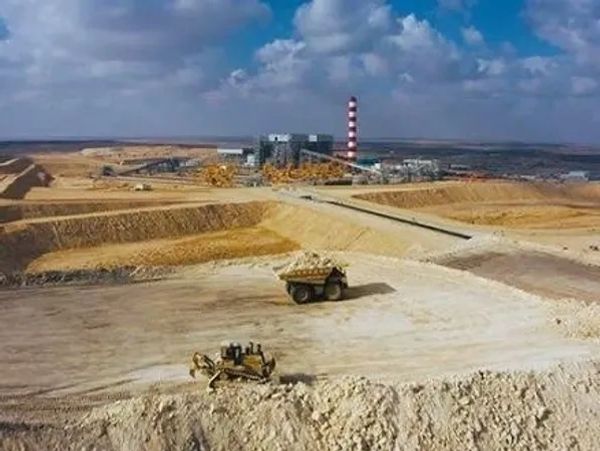 Open-pit mining site with industrial machinery and a factory in the background.