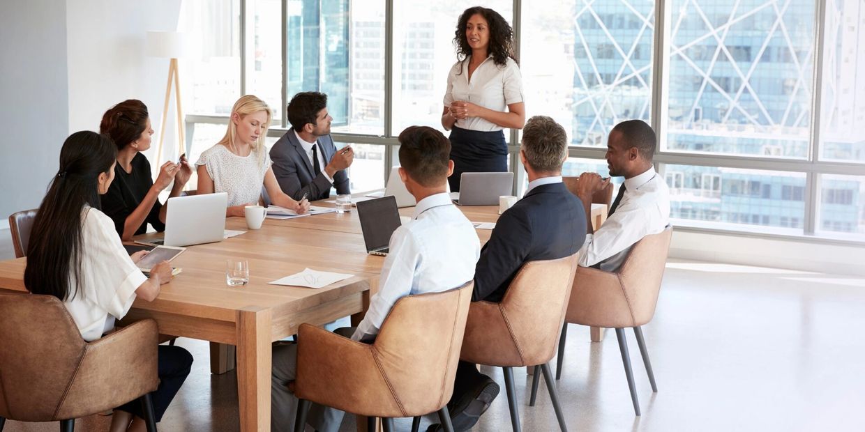 A woman leads a business meeting with attentive colleagues around a conference table.