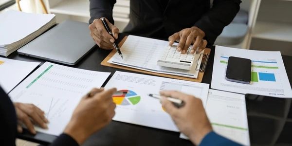 Two professionals analyzing financial charts with a calculator and documents on a desk.