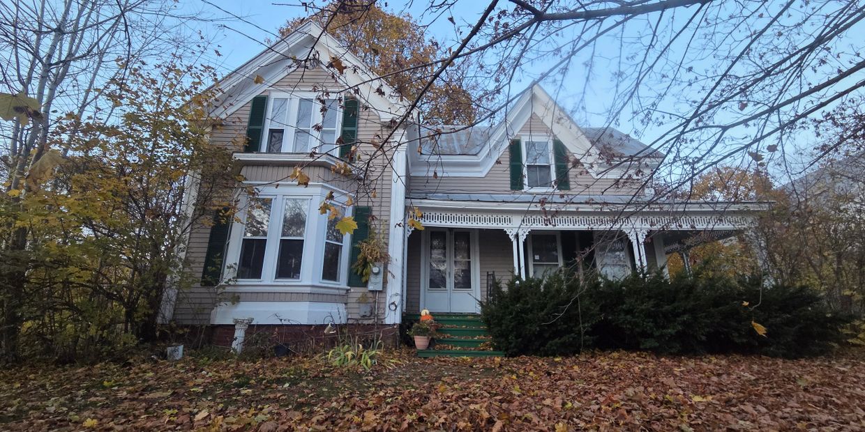 A large vintage house with green shutters surrounded by autumn foliage.