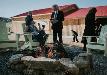 People dressed formally around a fire pit outdoors near wooden buildings.
