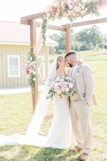 Bride and groom sharing a tender moment under a floral wedding arch outdoors.