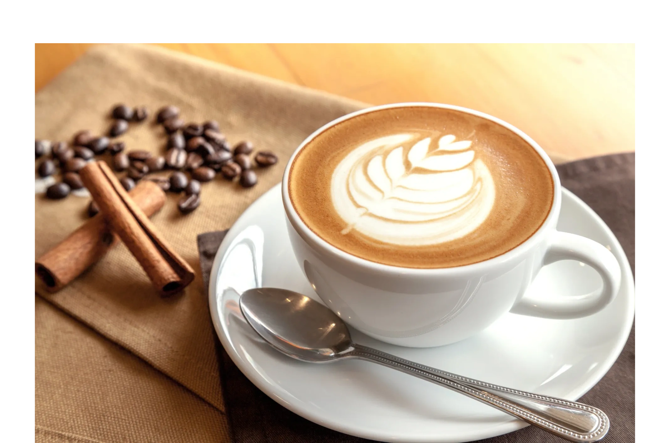 Cup of latte with coffee beans and cinnamon sticks.