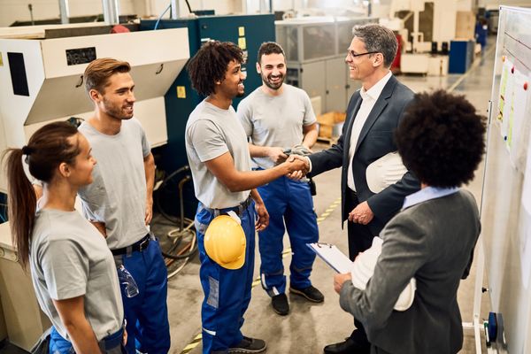 Workers shaking hands with a businessman in a factory.