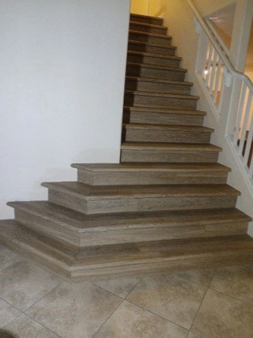 Wooden staircase with wide bottom steps and tiled floor.