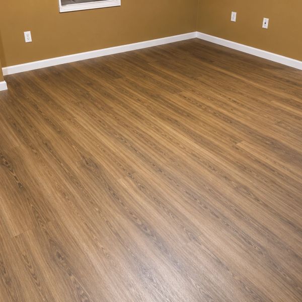 Empty room with wood-patterned vinyl flooring and tan walls.