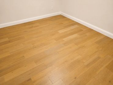 Empty room corner with light wooden floor and white walls.