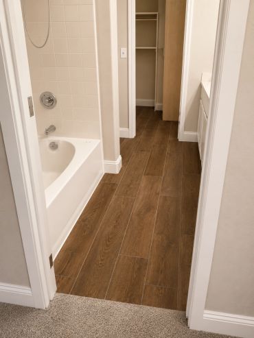 Bathroom with wood-look tile flooring and white bathtub.