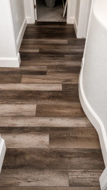 Curved white baseboard trim along a hallway with dark wood flooring.